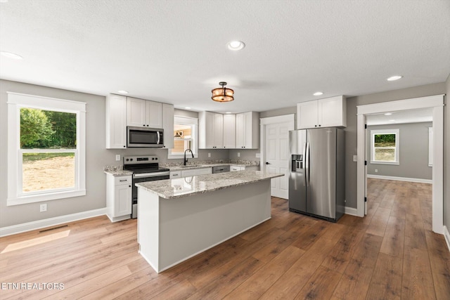 kitchen with light stone countertops, white cabinets, appliances with stainless steel finishes, and a center island