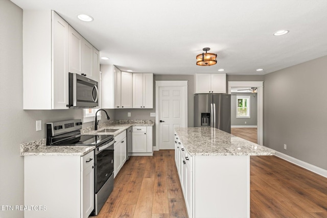 kitchen with a center island, sink, white cabinetry, stainless steel appliances, and light stone counters