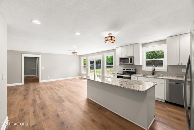 kitchen featuring a kitchen island, sink, stainless steel appliances, white cabinets, and light stone counters