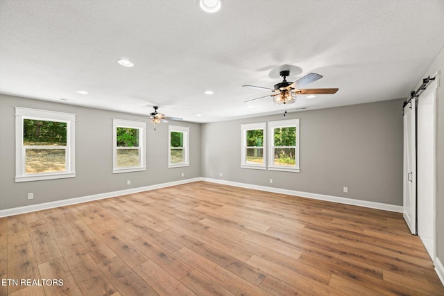 empty room with light hardwood / wood-style floors, ceiling fan, a textured ceiling, and a barn door