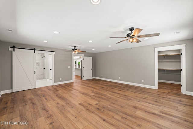 unfurnished living room featuring ceiling fan, a barn door, and wood-type flooring