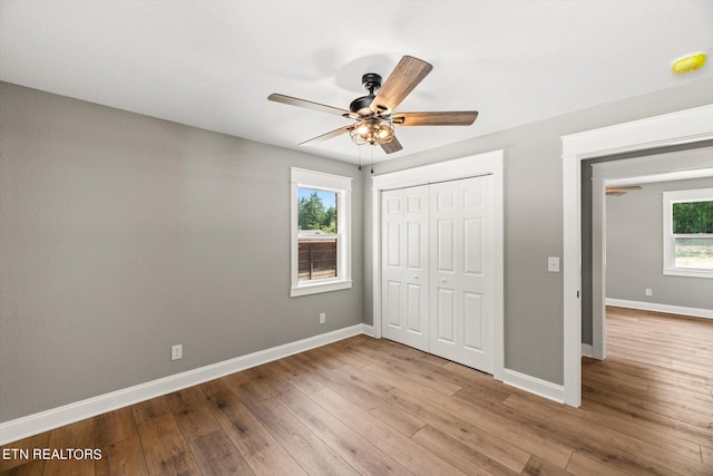 unfurnished bedroom with ceiling fan, a closet, multiple windows, and light hardwood / wood-style floors