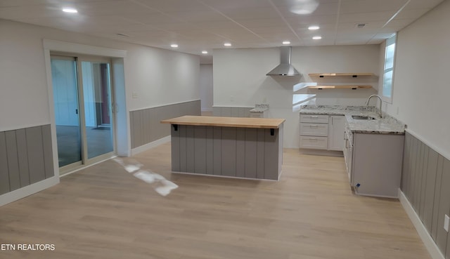 kitchen with a center island, sink, light wood-type flooring, white cabinets, and wall chimney exhaust hood