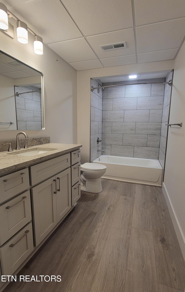 full bathroom with tiled shower / bath combo, a paneled ceiling, wood-type flooring, vanity, and toilet