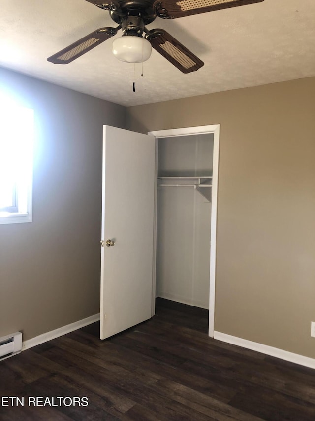 unfurnished bedroom featuring a baseboard heating unit, a closet, ceiling fan, and dark wood-type flooring