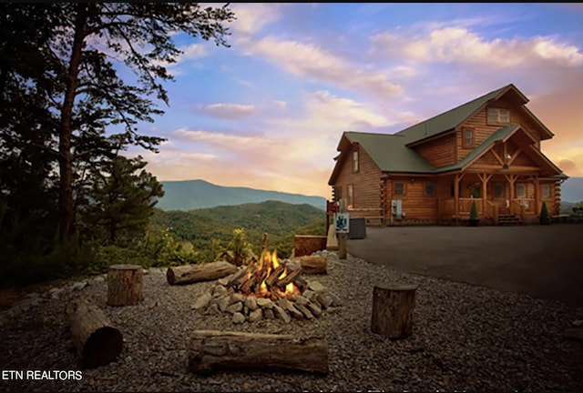 property exterior at dusk with a porch, a mountain view, and an outdoor fire pit