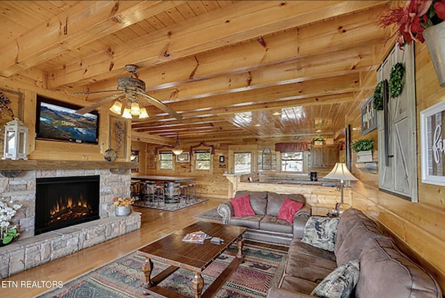 living room with a stone fireplace, wooden ceiling, hardwood / wood-style flooring, beam ceiling, and wood walls