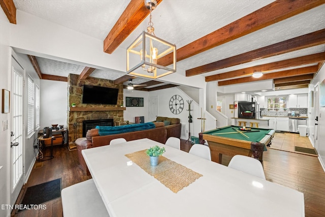 rec room with a textured ceiling, dark hardwood / wood-style flooring, beam ceiling, and a stone fireplace