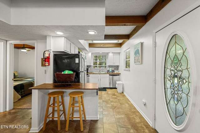 kitchen featuring a textured ceiling, white cabinets, stainless steel appliances, tasteful backsplash, and a breakfast bar