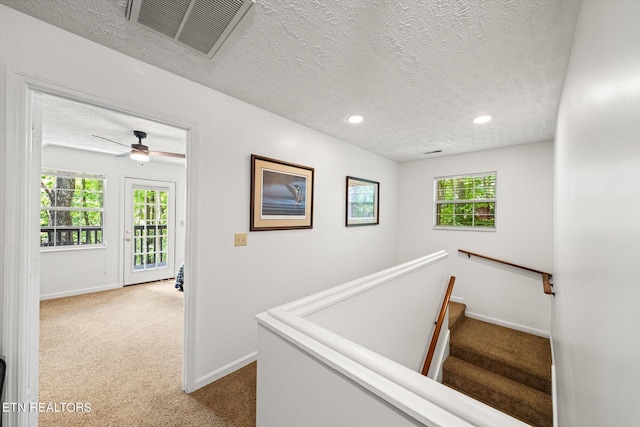 staircase with carpet floors, ceiling fan, and a textured ceiling