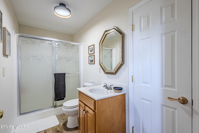 bathroom with toilet, a shower with shower door, hardwood / wood-style floors, and vanity