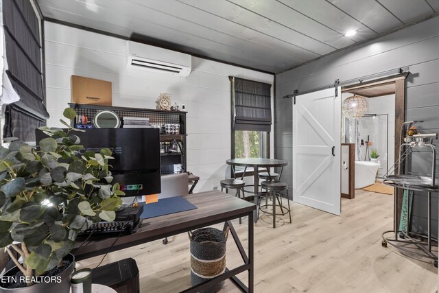 home office featuring a wall mounted air conditioner, wooden walls, a barn door, and light hardwood / wood-style flooring