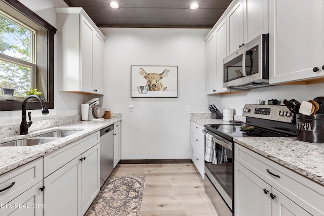 kitchen featuring stainless steel appliances, sink, white cabinetry, light stone counters, and light hardwood / wood-style flooring