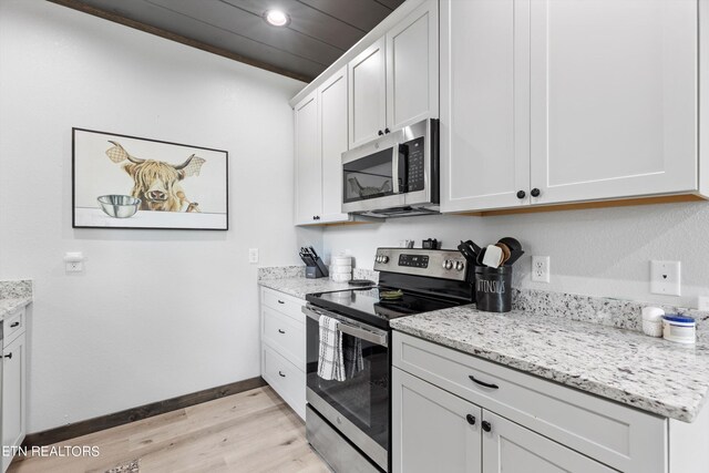 kitchen with stainless steel appliances, white cabinetry, light stone counters, and light hardwood / wood-style flooring