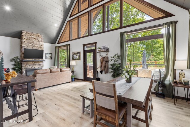 dining room with high vaulted ceiling, a fireplace, and light hardwood / wood-style flooring