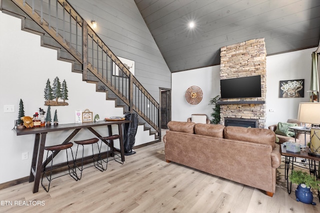 living room with high vaulted ceiling, a fireplace, and light wood-type flooring