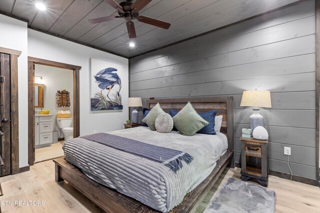 bedroom featuring light wood-type flooring, ceiling fan, wooden walls, and connected bathroom