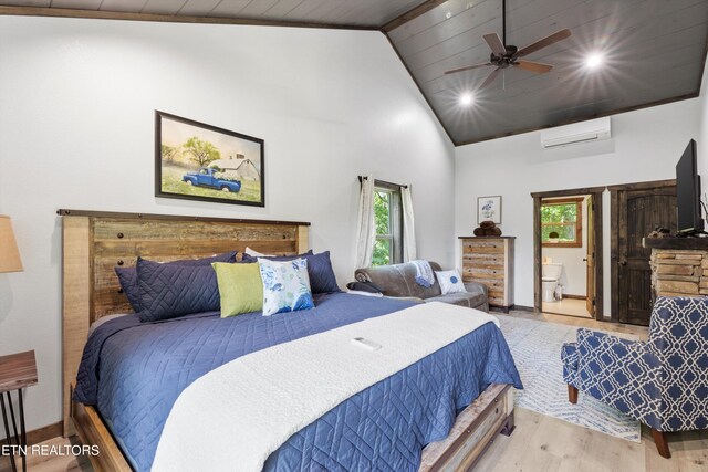 bedroom featuring wooden ceiling, ensuite bath, a wall mounted AC, ceiling fan, and light hardwood / wood-style flooring