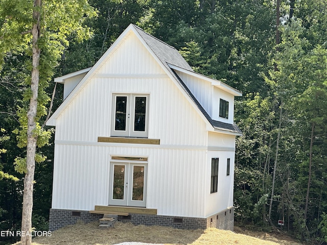 view of home's exterior with a shingled roof, crawl space, a view of trees, and french doors