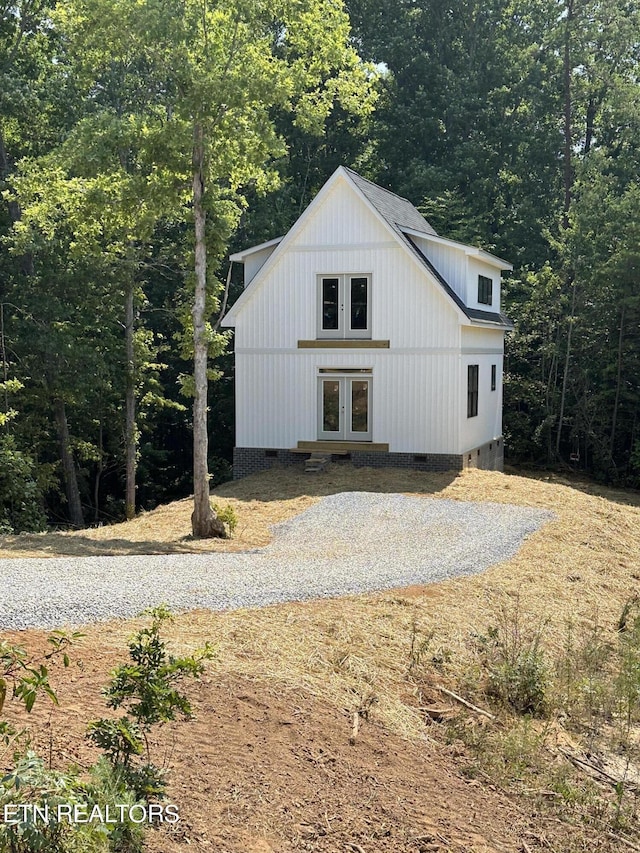 view of front of house featuring gravel driveway, crawl space, a view of trees, and french doors