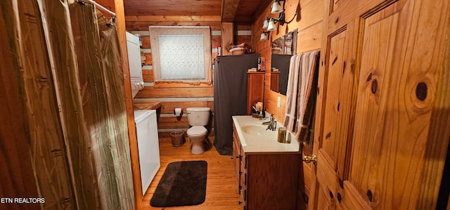 bathroom with wood-type flooring, vanity, toilet, wood walls, and stacked washing maching and dryer