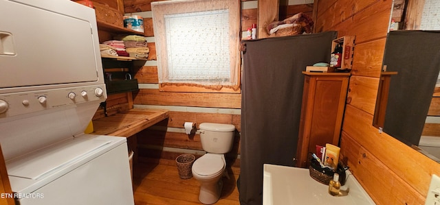 bathroom featuring stacked washer / drying machine, toilet, and wooden walls