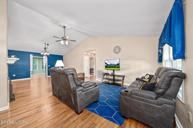 living room featuring ceiling fan with notable chandelier, hardwood / wood-style flooring, and vaulted ceiling