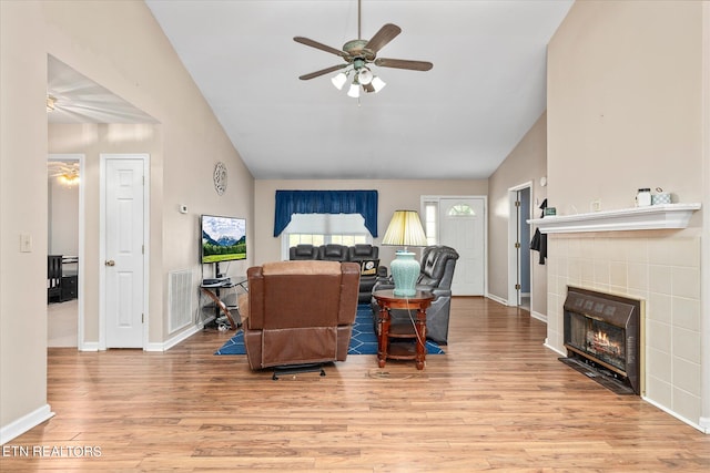 living room featuring lofted ceiling, a tiled fireplace, light wood-type flooring, and ceiling fan