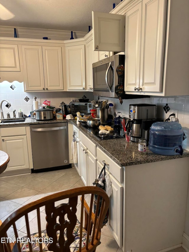 kitchen featuring dark stone countertops, light tile patterned floors, stainless steel appliances, decorative backsplash, and sink