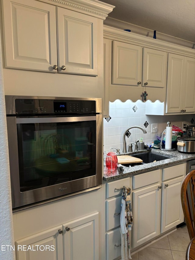 kitchen with light tile patterned floors, white cabinets, backsplash, oven, and sink