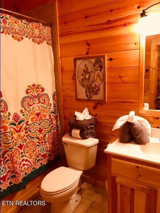 bathroom with tile patterned flooring, vanity, wooden walls, and toilet