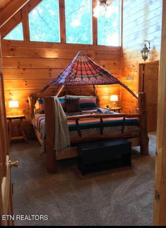 bedroom with wooden walls, high vaulted ceiling, and carpet flooring