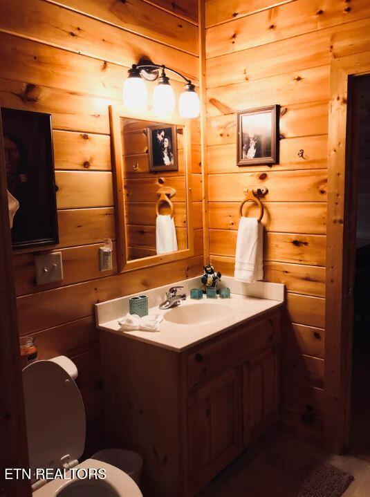 bathroom with vanity, toilet, and wood walls