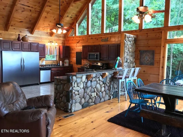 kitchen with wooden ceiling, appliances with stainless steel finishes, wooden walls, beamed ceiling, and ceiling fan