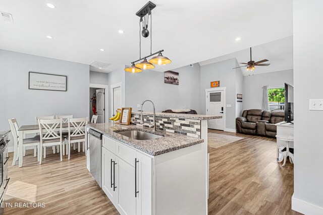 kitchen with sink, white cabinetry, a kitchen island with sink, hanging light fixtures, and light stone counters