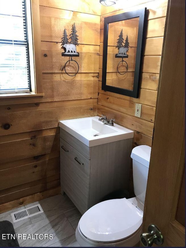 bathroom with toilet, vanity, and wooden walls