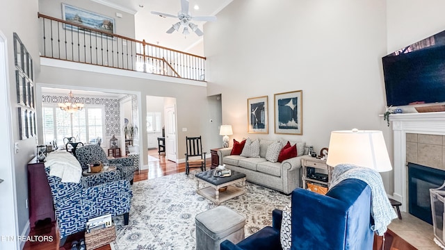 living room featuring ceiling fan with notable chandelier, a fireplace, and a towering ceiling