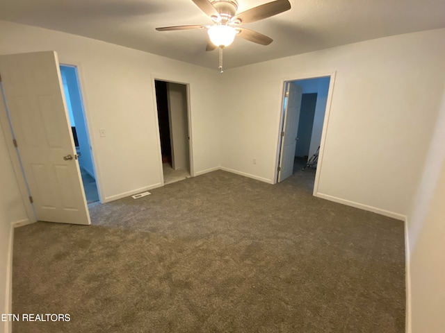 unfurnished bedroom featuring ensuite bathroom, dark colored carpet, and ceiling fan