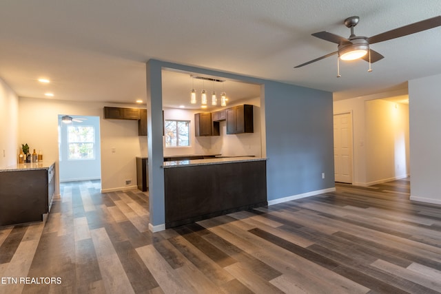 kitchen with light stone counters, dark brown cabinetry, dark hardwood / wood-style floors, a wall unit AC, and ceiling fan