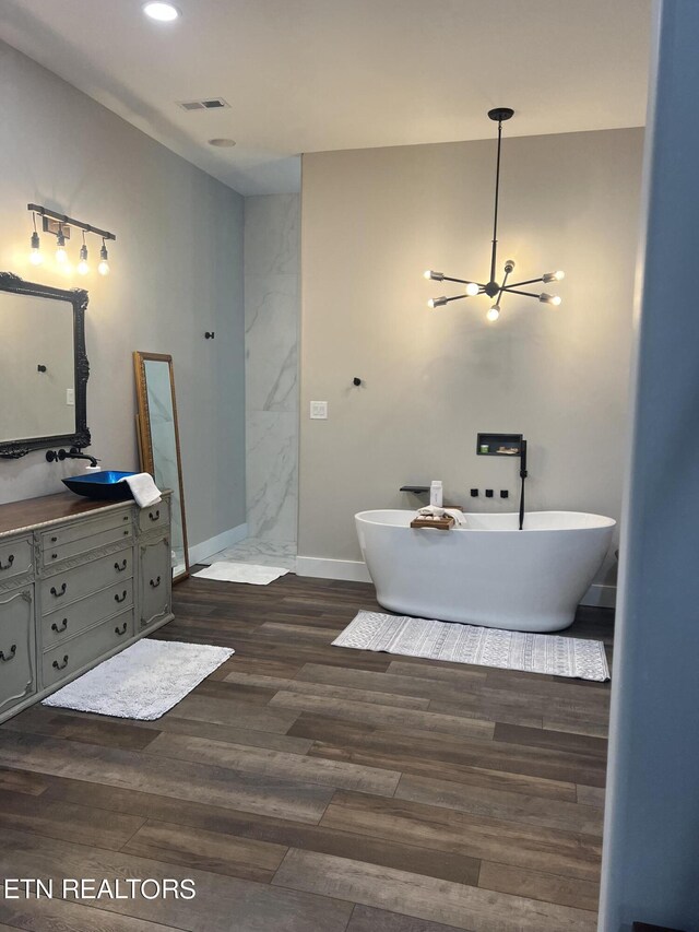 bathroom with hardwood / wood-style flooring, a tub to relax in, vanity, and an inviting chandelier