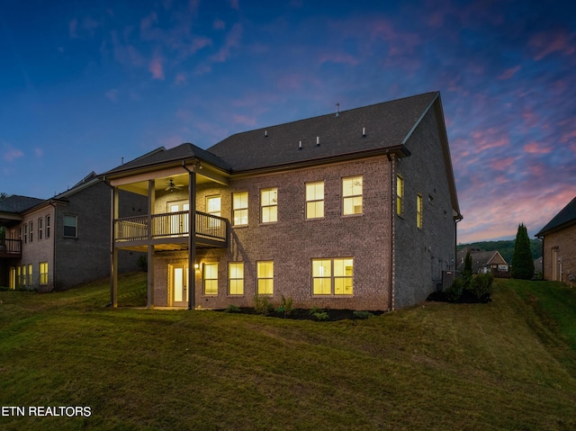 back house at dusk with ceiling fan, a yard, a balcony, and central air condition unit