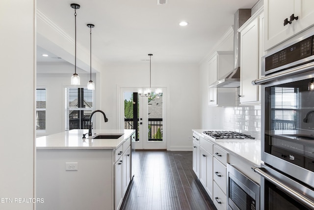 kitchen with sink, white cabinetry, hanging light fixtures, appliances with stainless steel finishes, and a kitchen island with sink