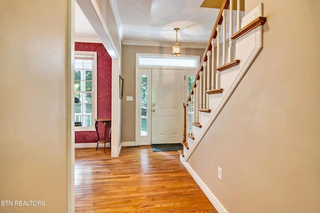 foyer entrance with light wood-type flooring, crown molding, and a textured ceiling