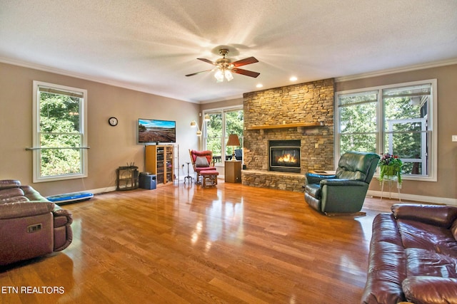 living room featuring ceiling fan, a fireplace, hardwood / wood-style flooring, ornamental molding, and a textured ceiling