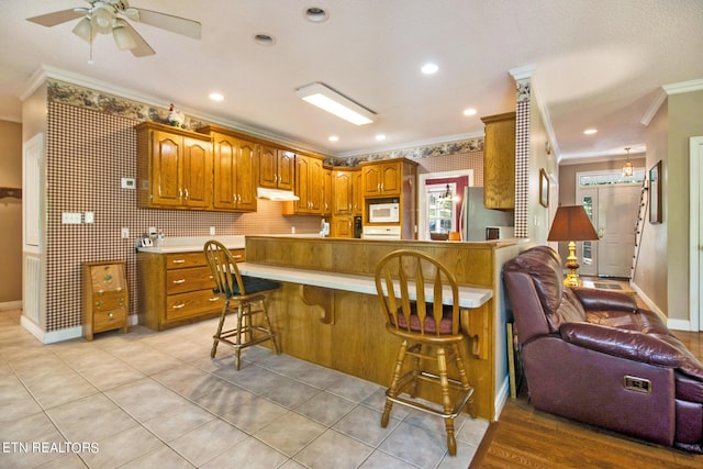 kitchen with a kitchen bar, kitchen peninsula, stainless steel refrigerator, light tile patterned floors, and crown molding