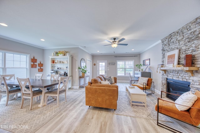 living room with crown molding, a stone fireplace, ceiling fan, and light hardwood / wood-style flooring