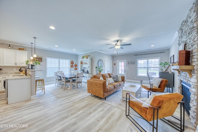 living room with sink, crown molding, light hardwood / wood-style flooring, ceiling fan, and a fireplace