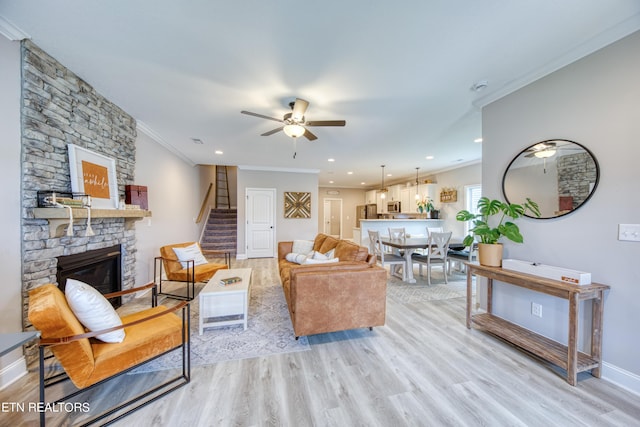 living room with crown molding, ceiling fan, a fireplace, and light wood-type flooring