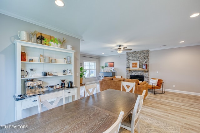 dining space featuring ceiling fan, ornamental molding, a stone fireplace, and light hardwood / wood-style flooring