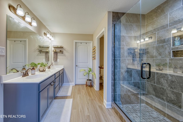 bathroom featuring hardwood / wood-style flooring, vanity, a shower with shower door, and a textured ceiling